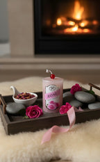 Candle labeled 'Rose' on a decorative tray with flowers and stones, fireplace in the background